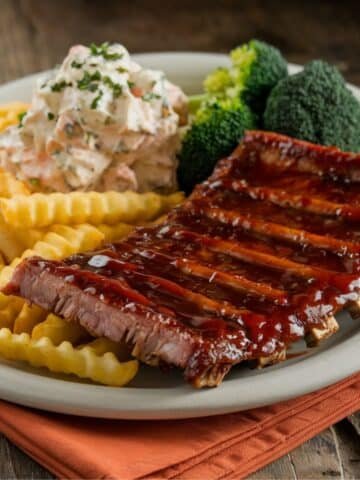 Juicy Boneless Beef Ribs glazed with barbecue sauce, served with crinkle-cut fries, creamy coleslaw, and steamed broccoli on a rustic plate – perfect for a delicious Boneless Beef Ribs Recipe meal.