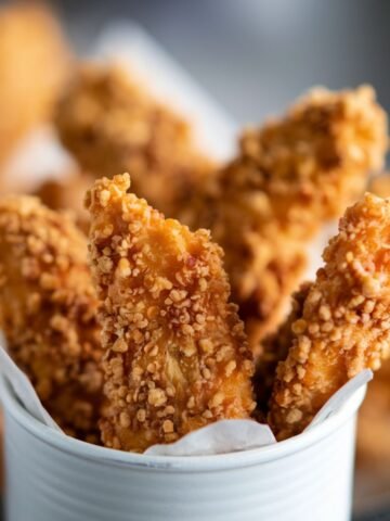 rispy golden chicken tenders served in a white container, representing a Copycat Cane’s Chicken Recipe with a crunchy coating and tender, juicy interior.