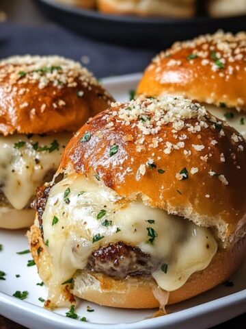 Homemade garlic parmesan cheeseburger bombs with melted cheese, golden buns, and a sprinkle of herbs, served on a white plate.