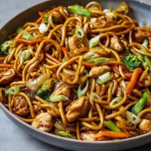 Chicken Lo Mein Recipe in a skillet with glossy noodles, tender chicken pieces, broccoli florets, carrots, onions, and scallions tossed in a rich soy-based sauce - perfectly caramelized and ready to serve, showing real home-cooked texture and freshness.