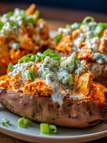 Homemade Buffalo Chicken Stuffed Sweet Potatoes on a white plate, topped with ranch, blue cheese, and green onions, warm natural light, homemade and cozy.