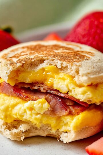 Homemade Egg Mcmuffin Recipe in 5 Easy Steps 21 Egg Mcmuffin Recipe A delicious homemade egg McMuffin on a plate, with the sandwich taking a bite to reveal the melted cheese, Canadian bacon, and scrambled eggs inside