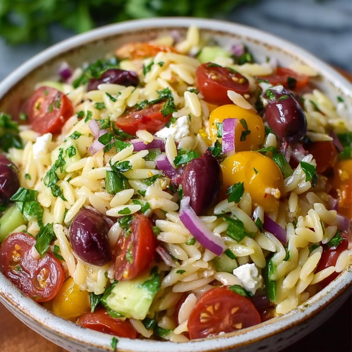 Healthy Greek Orzo Salad Recipe 9 A bowl of Greek orzo salad filled with cherry tomatoes, cucumbers, Kalamata olives, red onions, parsley, and crumbled feta cheese