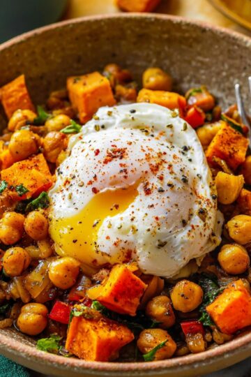 Easy Sweet Potato Hash Recipe | 5 Simple Ingredients 22 Sweet Potato Hash A close-up shot of a sweet potato chickpea hash topped with a poached egg, visible spices and herbs, fork resting in the bowl, shallow depth of field, cozy brunch vibe, professional food photography.