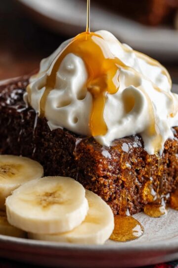 Easy Gingerbread Cake Recipe | Moist & Perfectly Spiced 24 gingerbread cake A slice of moist gingerbread cake topped with whipped cream and honey drizzle, served with banana slices on a plate.