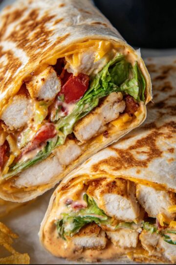 30-Minute Grilled Chicken Burrito - Crispy & Cheesy 17 grilled chicken burrito Chipotle ranch grilled chicken burrito cut in half showing juicy chicken, melted cheese, lettuce, tomatoes, and creamy chipotle ranch sauce inside a toasted tortilla.