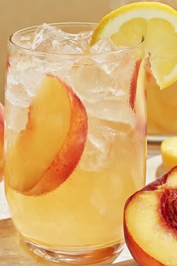 Peach Lemonade Recipe: Fresh, Easy & Ready in Minutes 28 peach lemonade A refreshing glass of peach lemonade filled with ice and garnished with lemon slices and mint leaves. Peaches and lemons are placed beside the glass on a white surface