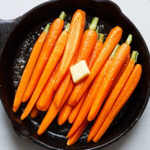 Best 5-Ingredient Brown Sugar Glazed Carrots Recipe 16 A skillet filled with uncooked carrots arranged neatly, waiting to be cooked. The butter is already added to the skillet, with the carrots sitting in a base of melted butter. The warm orange color of the carrots contrasts beautifully with the shiny butter.