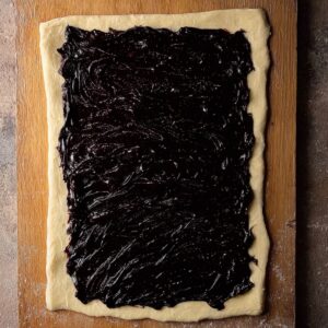 Best Babka Recipe | Chocolate Orange Swirl Bread 18 Rolled-out enriched dough rectangle evenly spread with dark chocolate filling, placed on a wooden board, clean edges, top-down food photography, rustic kitchen setting, matte natural light