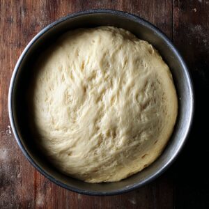 Best Babka Recipe | Chocolate Orange Swirl Bread 16 A large metal bowl filled with risen enriched dough, doubled in size, smooth and airy texture visible, rustic wooden table background, natural ambient light, overhead shot