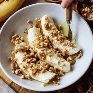 Easy Banana Bread Recipe - Ready in 70 Minutes | So Moist 15 A spatula is stirring flour into a banana bread mixture in a glass bowl. The flour is being folded into the wet ingredients, with eggs and bananas in the background.