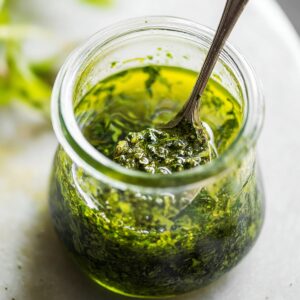 Delicious Burrata Salad Beet Recipe 15 A close-up of a small glass jar filled with vibrant green walnut basil oil, with a spoon stirring the fragrant dressing, perfect for adding flavor to salads and vegetables.