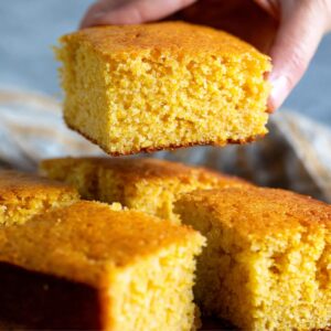 Cornbread Recipe: Easy 40-Minute Homemade Version 17 "A hand picking up a square of freshly baked cornbread, showcasing the soft, fluffy texture and golden crust."