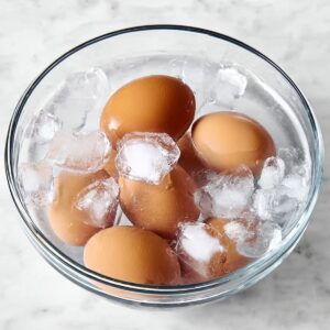 Deviled Eggs Recipe - Perfect in 35 Minutes or Less! 16 A clear glass bowl filled with ice and water, holding several brown eggs that are cooling down after boiling. The ice cubes are clearly visible around the eggs.