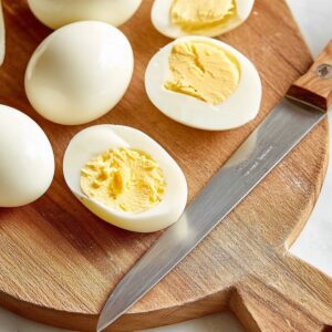Deviled Eggs Recipe - Perfect in 35 Minutes or Less! 17 A wooden cutting board with a knife resting next to a hard-boiled egg that has been sliced in half. The egg whites are visible with the yolk removed, and a small bowl contains the egg yolk.