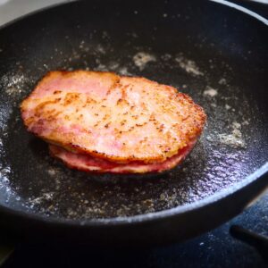 Homemade Egg Mcmuffin Recipe in 5 Easy Steps 16 Canadian bacon cooking in a hot pan, sizzling and developing a crispy texture as it browns