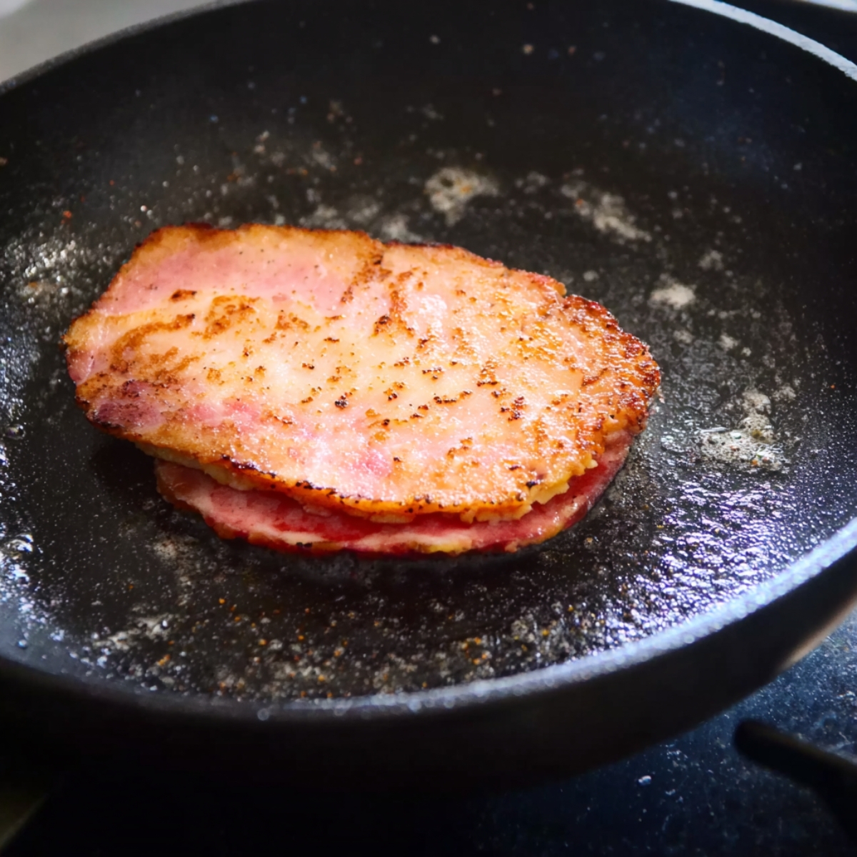 Homemade Egg Mcmuffin Recipe in 5 Easy Steps 11 Canadian bacon cooking in a hot pan, sizzling and developing a crispy texture as it browns