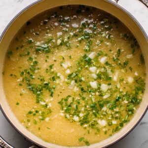 The Best French Garlic Soup Recipe 15 A simmering pot of French garlic soup with visible pieces of garlic and chopped herbs floating in a golden broth.