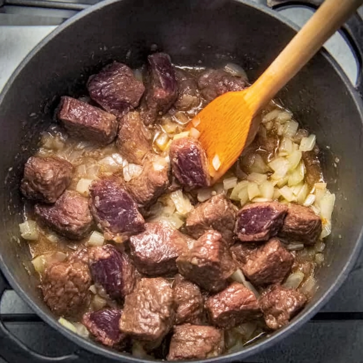 Easy Hungarian Goulash Recipe | Traditional Paprika Beef 10 Overhead view of beef cubes browning with chopped onions in a pot, stirred with a wooden spoon during the early cooking stage.