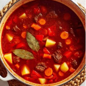 Easy Hungarian Goulash Recipe | Traditional Paprika Beef 16 Close-up of a rustic beef stew with tender meat, potatoes, carrots, and herbs simmering in a rich red paprika-based broth.