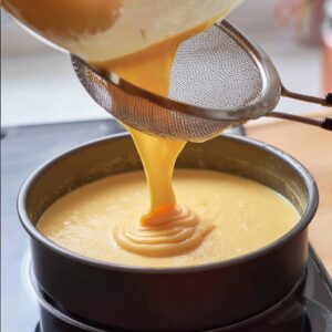 Filipino Leche Flan Recipe (Silky & Easy!) - 5 Ingredients 17 Smooth egg custard being poured through a fine mesh strainer into a round baking pan.