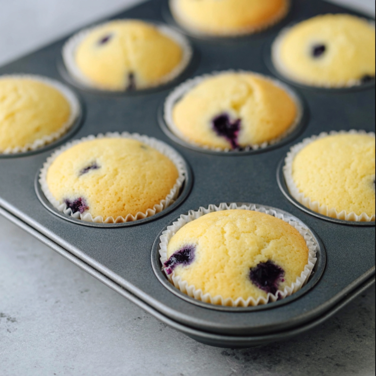 Lemon Blueberry Cupcakes Recipe (Moist & Easy!) 12 Top-down view of lemon cupcake batter with fresh blueberries folded in using a silicone spatula inside a stainless steel mixing bowl.