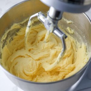 Lemon Blueberry Cupcakes Recipe (Moist & Easy!) 15 Lemon cupcake batter being mixed in a stand mixer with a metal beater, showing a smooth, creamy, pale yellow texture.