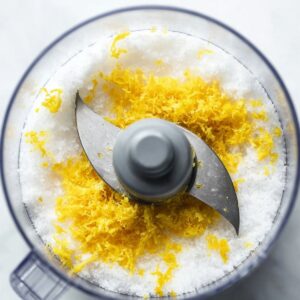 Best Lemon Cheesecake Recipe 16 Overhead view of a food processor filled with granulated sugar and fresh lemon zest before mixing.