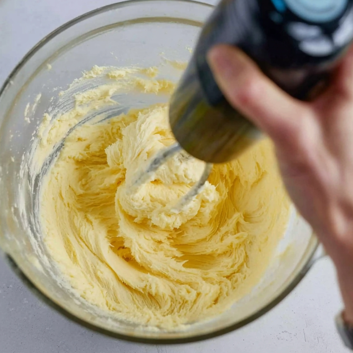 Lemon Meltaway Cookies Recipe (Ready in 33 Minutes!) 11 "A person using an electric mixer to blend ingredients in a large glass mixing bowl. The dough for lemon meltaway cookies is in the early stages, with a light and fluffy consistency."
