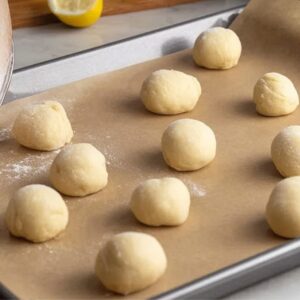 Lemon Meltaway Cookies Recipe (Ready in 33 Minutes!) 17 "Freshly rolled dough balls for lemon meltaway cookies, placed on a parchment-lined baking sheet. Lemons are visible in the background, hinting at the citrusy flavor of the cookies.""Freshly rolled dough balls for lemon meltaway cookies, placed on a parchment-lined baking sheet. Lemons are visible in the background, hinting at the citrusy flavor of the cookies."