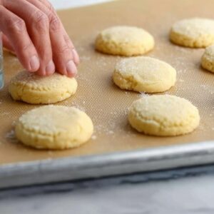 Lemon Meltaway Cookies Recipe (Ready in 33 Minutes!) 18 "Freshly rolled dough balls for lemon meltaway cookies, placed on a parchment-lined baking sheet. Lemons are visible in the background, hinting at the citrusy flavor of the cookies."