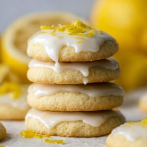Lemon Meltaway Cookies Recipe (Ready in 33 Minutes!) 19 "A stack of three lemon meltaway cookies with a glossy lemon icing, garnished with fresh lemon zest. The cookies are soft and tender, with a blurred background of lemons and other cookies."