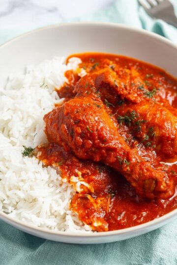 Nigerian Chicken Stew 18 A bowl of Nigerian red stew served over fluffy white rice, rich deep red tomato pepper sauce coating tender chicken pieces, clean white background, soft natural light, minimal food styling, close-up food photography