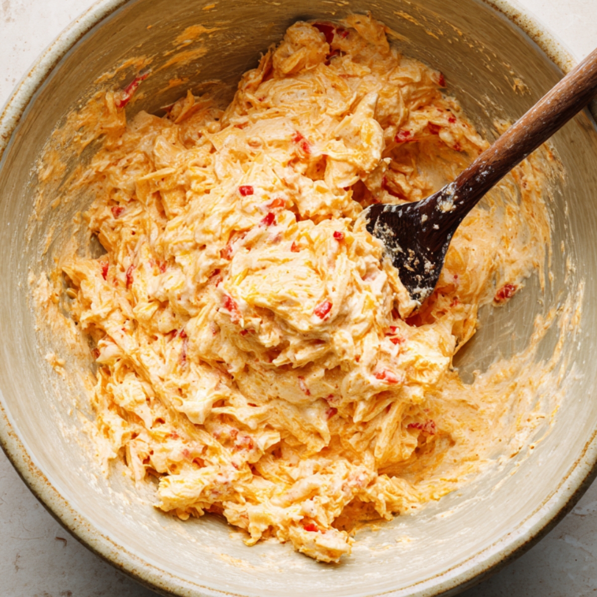 The Best Pimento Cheese Recipe 11 “A bowl filled with freshly mixed pimento cheese, with a wooden spoon stirring the creamy blend of shredded cheese and diced pimentos.