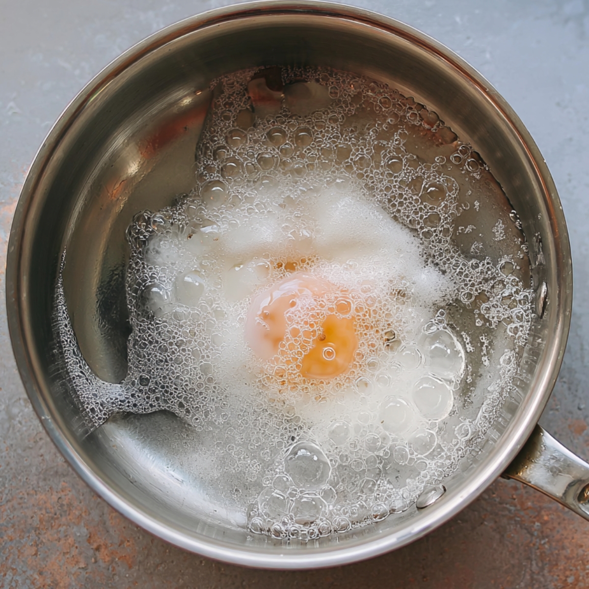 Easy Sweet Potato Hash Recipe | 5 Simple Ingredients 11 A minimal overhead shot of a poached egg cooking in gently simmering water inside a stainless steel saucepan, bubbles forming around the egg white, clean kitchen aesthetic, soft natural lighting, realistic food photography.