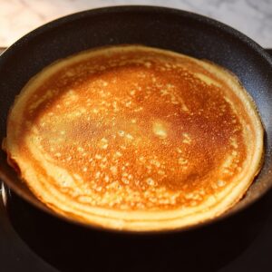 Tiramisu Crepe Cake Recipe | Easy 6-Step Guide 14 A perfectly golden crepe cooking in a nonstick skillet. The crepe shows a slightly crispy edge with a smooth, even surface.