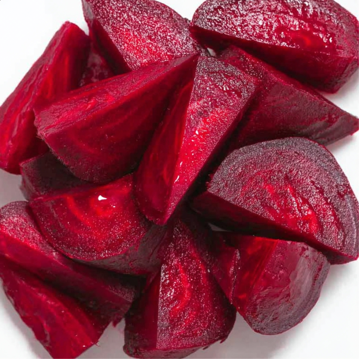 How to Make Beetroot Juice at Home - 2 Easy Ways 10 Top-down view of freshly cooked or raw beet chunks cut into wedges, vibrant red color, glossy texture, arranged closely on a white background.