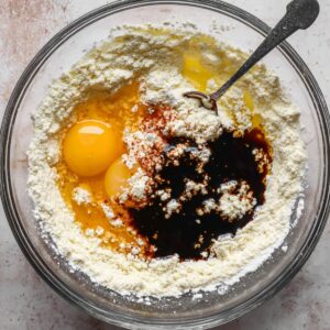 Easy Gingerbread Cake Recipe | Moist & Perfectly Spiced 15 Top-down view of a glass bowl with flour, eggs, vanilla extract, and spices being mixed for gingerbread cake batter.