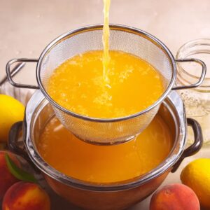 Peach Lemonade Recipe: Fresh, Easy & Ready in Minutes 16 A fine mesh strainer filled with freshly strained peach lemonade. The liquid is flowing into a bowl below, with mason jars and fresh peaches and lemons surrounding the setup