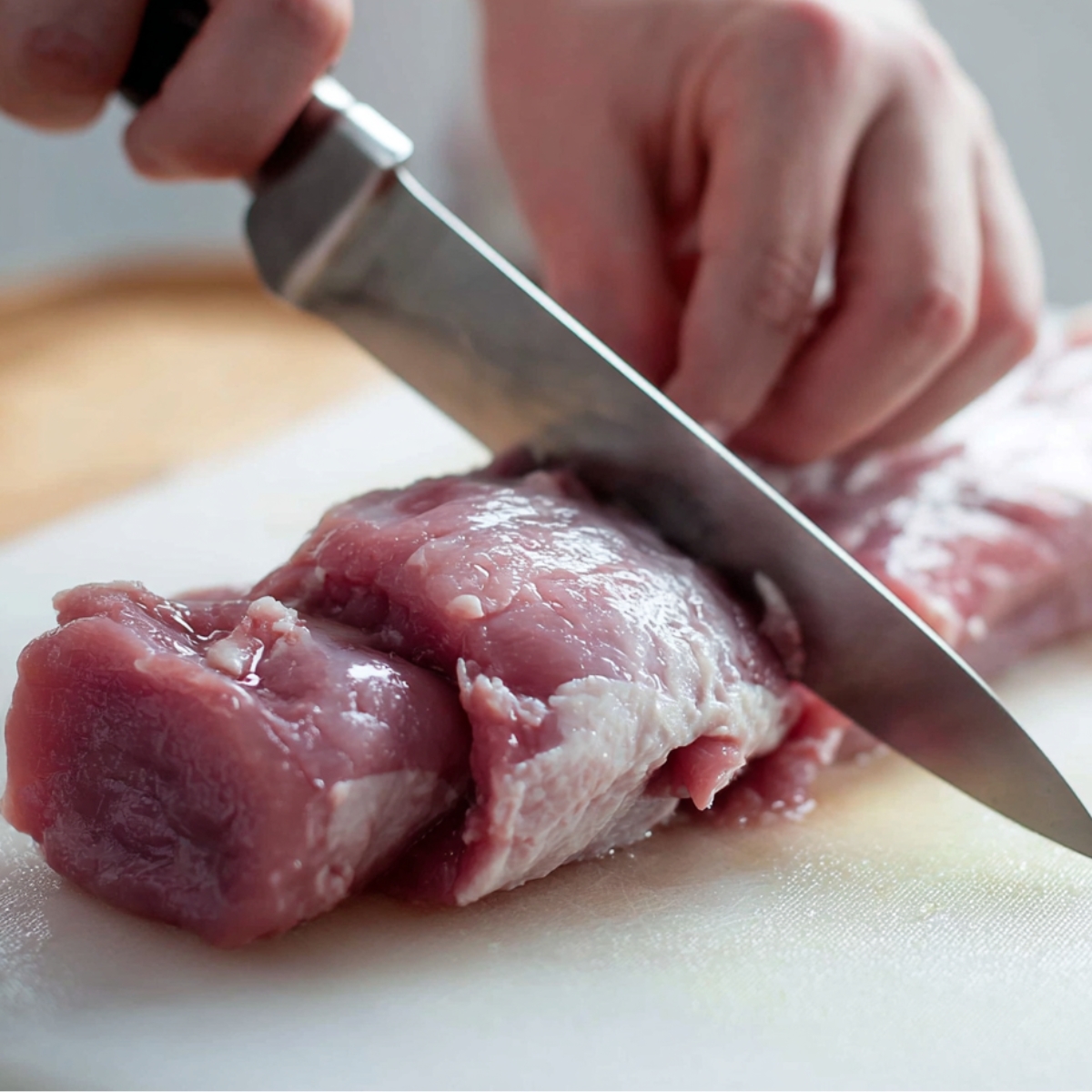 Best Pork Tenderloin Recipe | 30-Minute Dinner 11 Hands trimming raw pork tenderloin with a sharp knife on a cutting board, removing the silver skin during meat preparation.