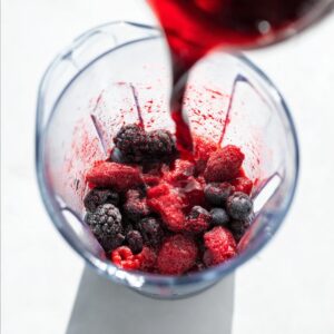 5-Minute Red Wine Slushies Recipe | Frozen Sangria 13 Red wine being poured over frozen mixed berries inside a blender, preparing a berry wine slushie