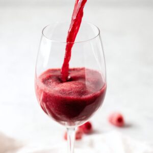 5-Minute Red Wine Slushies Recipe | Frozen Sangria 14 Red wine slushie being poured into a clear wine glass, smooth frozen texture on a white background