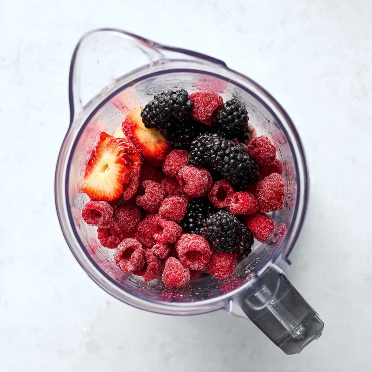 5-Minute Red Wine Slushies Recipe | Frozen Sangria 10 Frozen mixed berries including raspberries, blackberries, and strawberries inside a blender jar on a white background