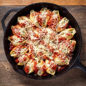 7-Step Sausage Stuffed Shells That'll Make Your Family 18 Top view of sausage stuffed jumbo pasta shells topped with marinara and shredded mozzarella in a cast iron skillet