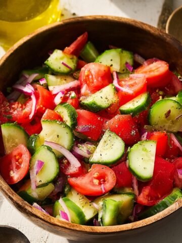 Homemade Cucumber Tomato Salad with red onion, seasoned with black pepper, in a wooden bowl, with a drizzle of olive oil.