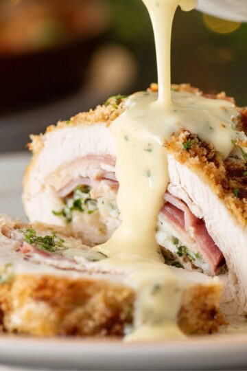 Baked Chicken Cordon Bleu Recipe | Crispy & Easy 16 Chicken Cordon Bleu Sliced chicken cordon bleu showing layers of chicken, ham, and melted cheese, topped with creamy Dijon sauce being poured over the top