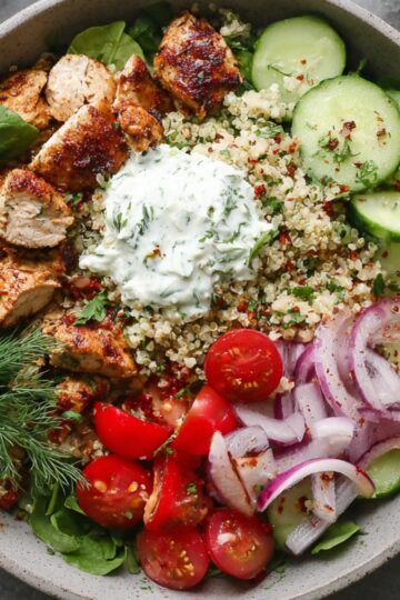 Healthy Greek Bowl Recipe with Chicken & Tzatziki (35 Min) 15 Greek bowl recipe with grilled chicken, quinoa, cucumber slices, cherry tomatoes, red onion, leafy greens, and creamy tzatziki sauce topped with fresh dill