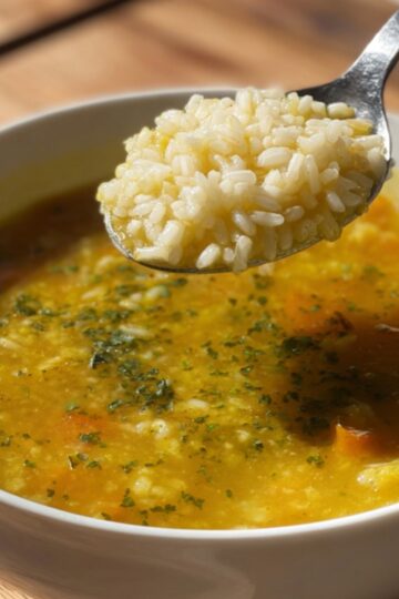 Italian Penicillin Soup Recipe 14 Italian Penicillin Soup Close-up of a bowl of golden vegetable soup with rice, spoon lifting cooked rice from the soup, warm natural light