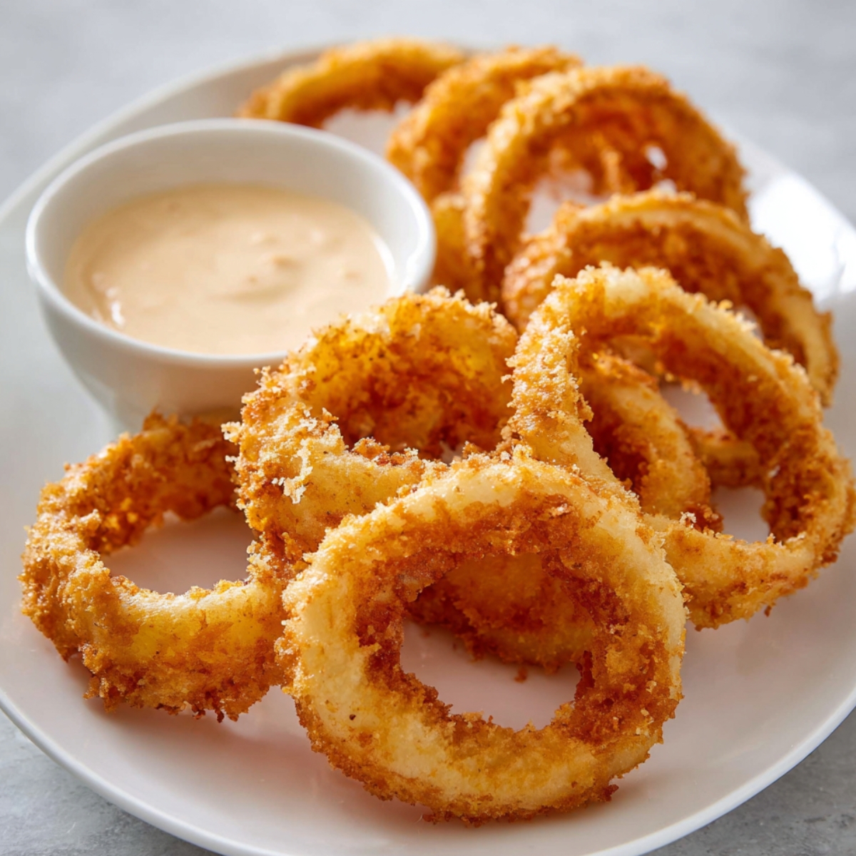 Onion Rings Recipe Golden crispy onion rings served on a white plate with creamy dipping sauce in a small bowl, crunchy texture visible, restaurant-style plating, bright natural light, high-resolution food photography.