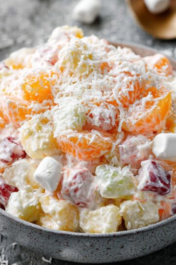 Ambrosia Fruit Salad Recipe 9 ambrosia fruit salad Finished ambrosia salad served in a gray ceramic bowl, creamy fruit salad with mandarin oranges, pineapple, cherries, coconut, and mini marshmallows, styled food photography, soft daylight, textured stone background, scattered marshmallows, professional food blog look, ultra realistic”